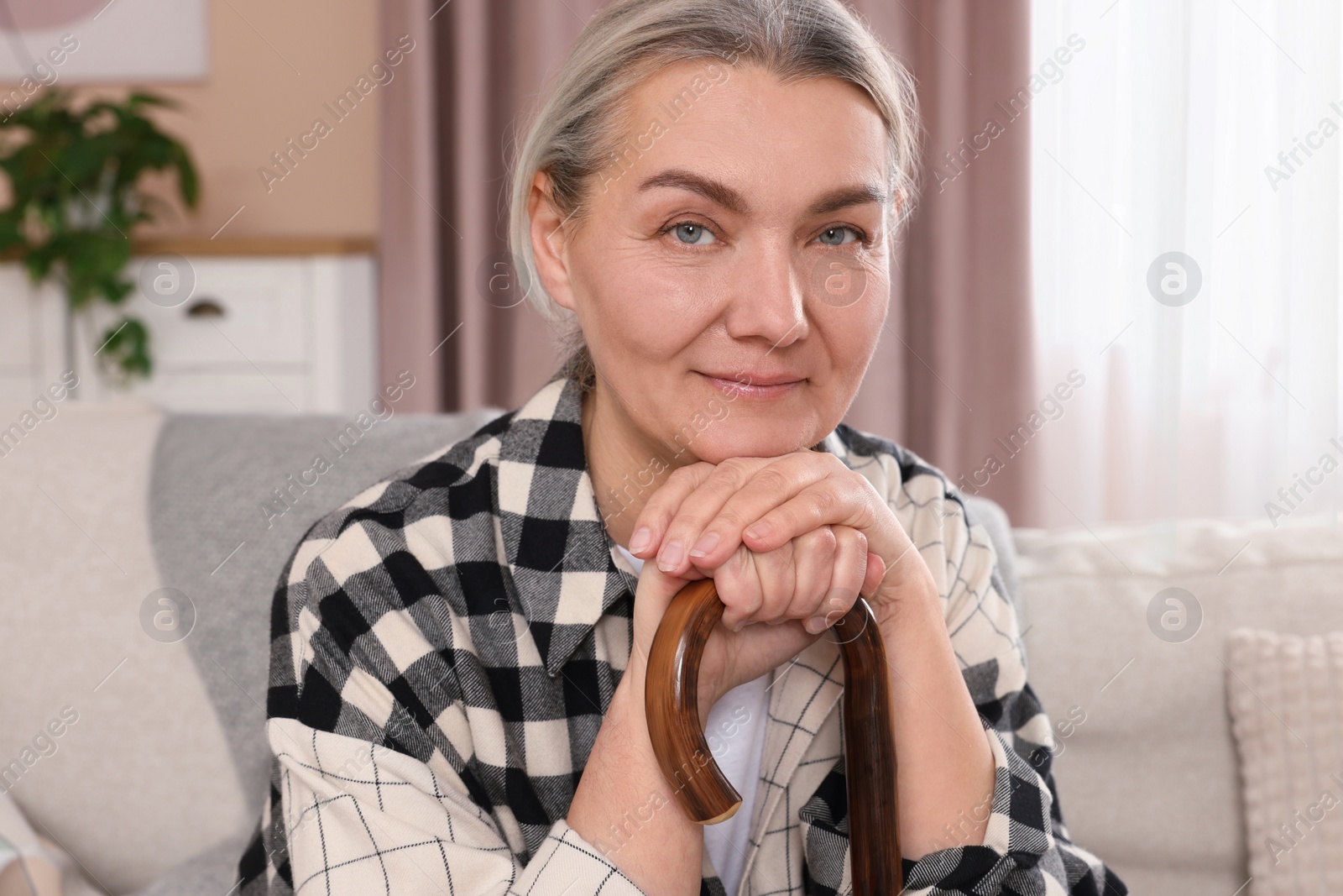 Photo of Senior woman with walking cane sitting on sofa at home