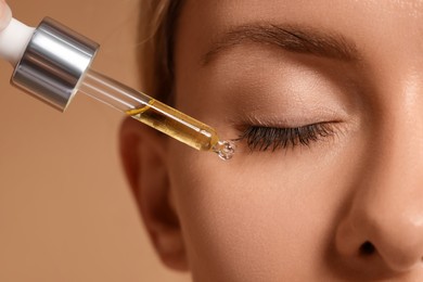 Woman applying cosmetic serum onto her face on beige background, closeup