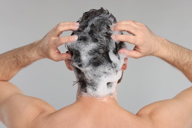 Man washing his hair with shampoo on grey background, back view