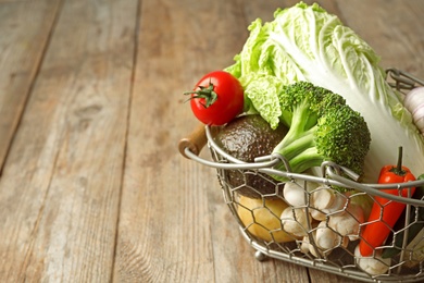 Photo of Fresh vegetables in metal basket on wooden table. Space for text
