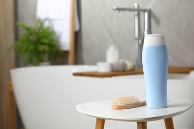 Bottle of shampoo and wooden hairbrush on white table in bathroom, space for text