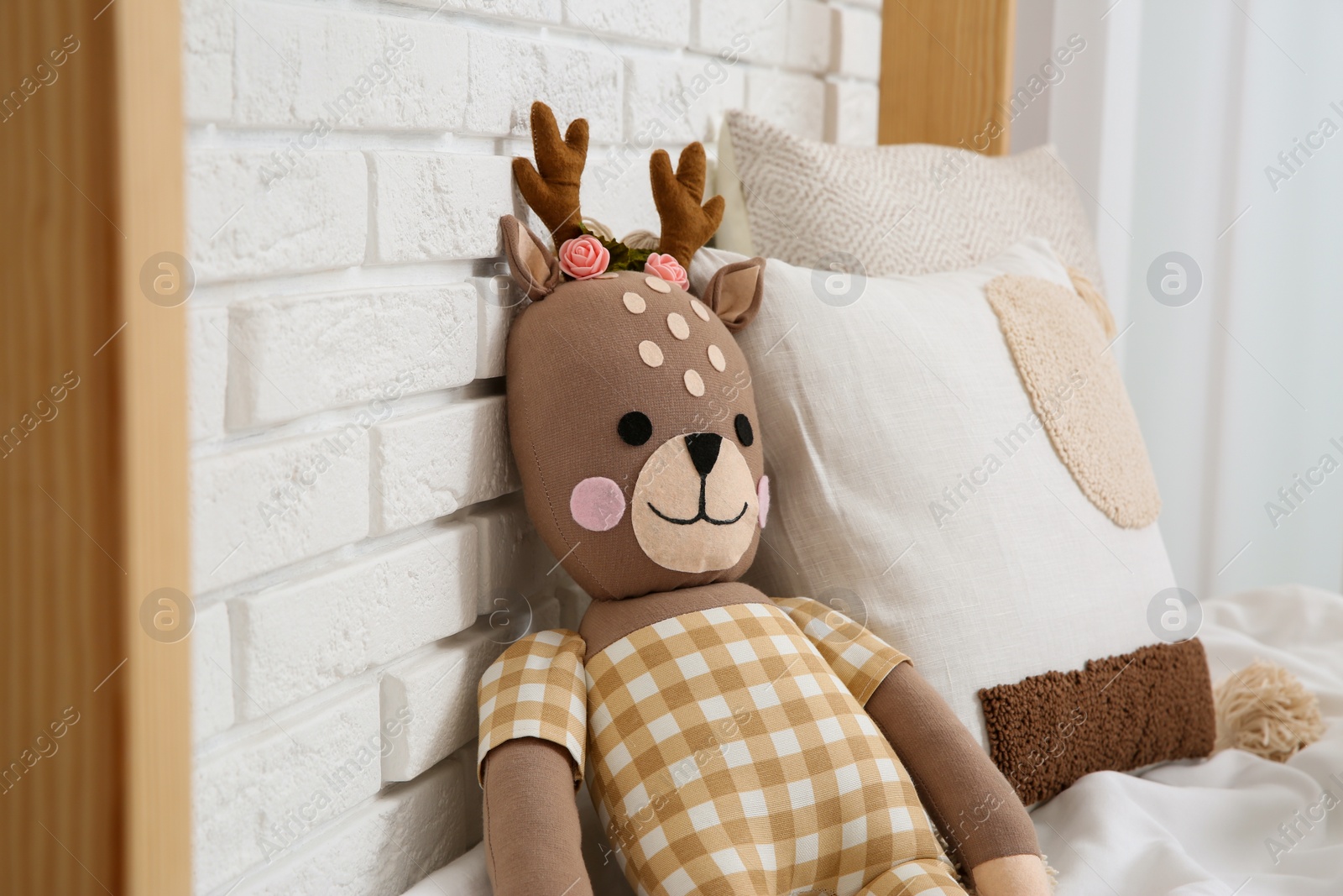 Photo of Toy deer on bed near white brick wall. Children's room interior design