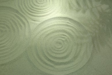 Photo of Beautiful spirals and shadows of leaves on sand, above view. Zen garden