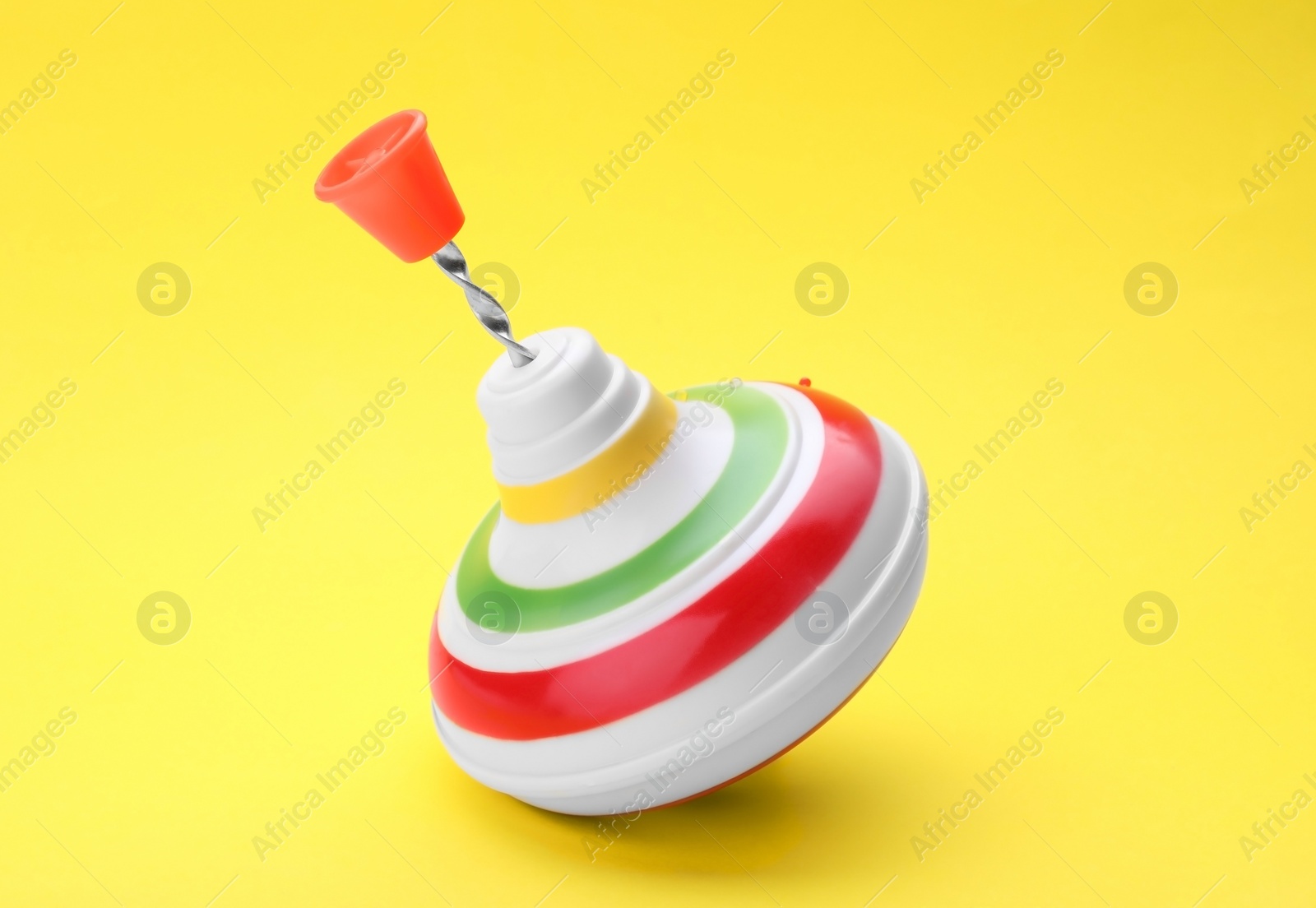 Photo of One bright spinning top on yellow background, closeup. Toy whirligig