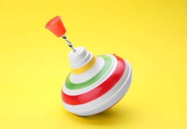 Photo of One bright spinning top on yellow background, closeup. Toy whirligig