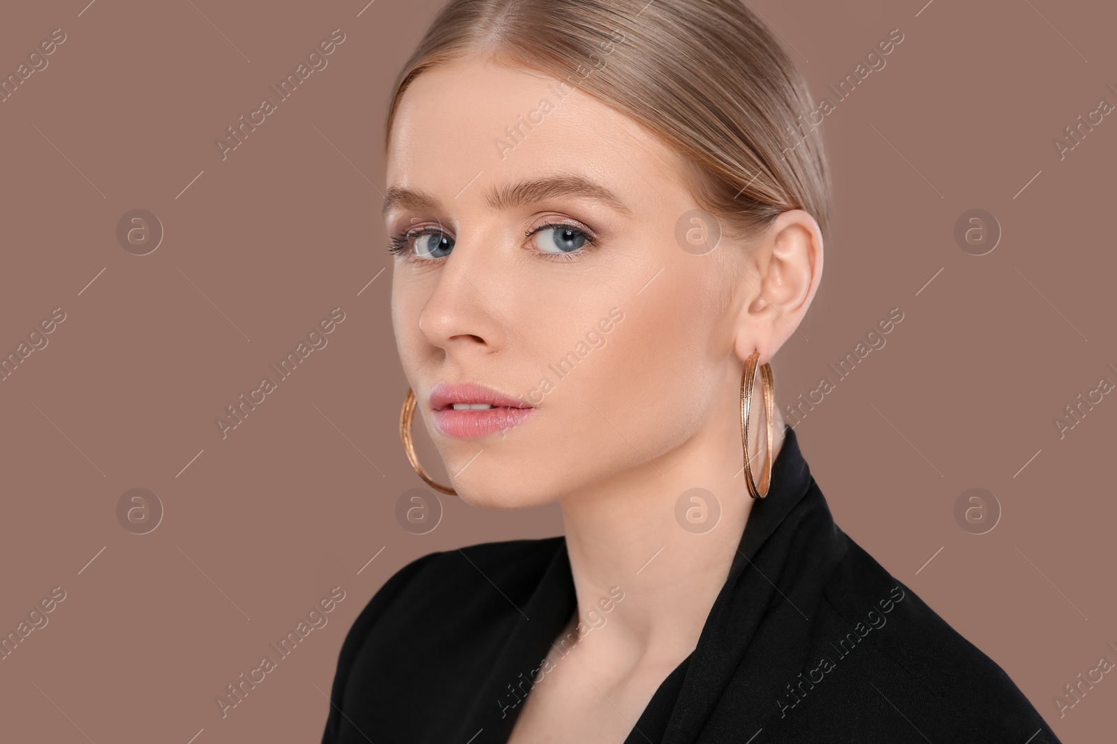 Photo of Beautiful young woman with elegant earrings on light brown background