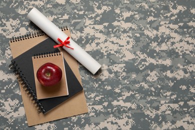 Photo of Notebooks, apple and diploma on camouflage background, flat lay with space for text. Military education