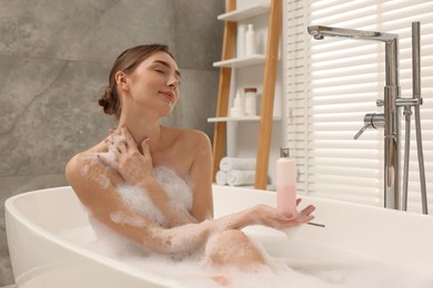 Photo of Woman taking bath with shower gel in bathroom