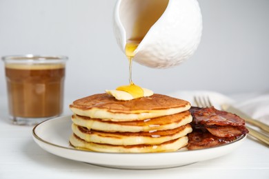 Photo of Pouring maple syrup onto delicious pancakes with butter and fried bacon at white wooden table, closeup