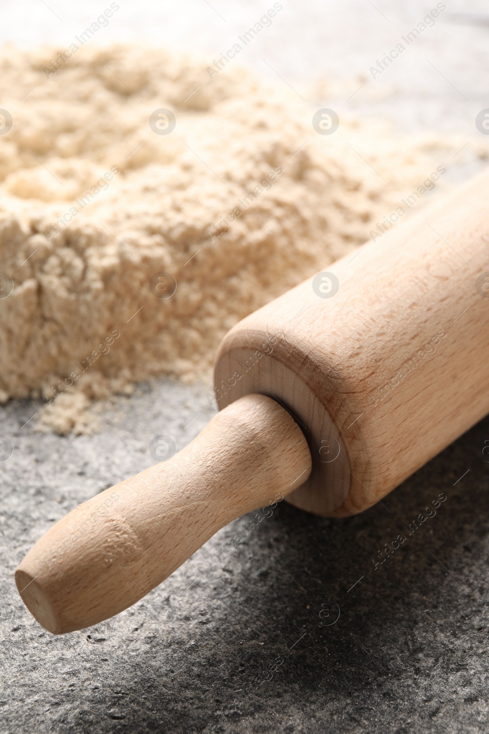 Photo of Rolling pin and scattered flour on grey textured table, closeup