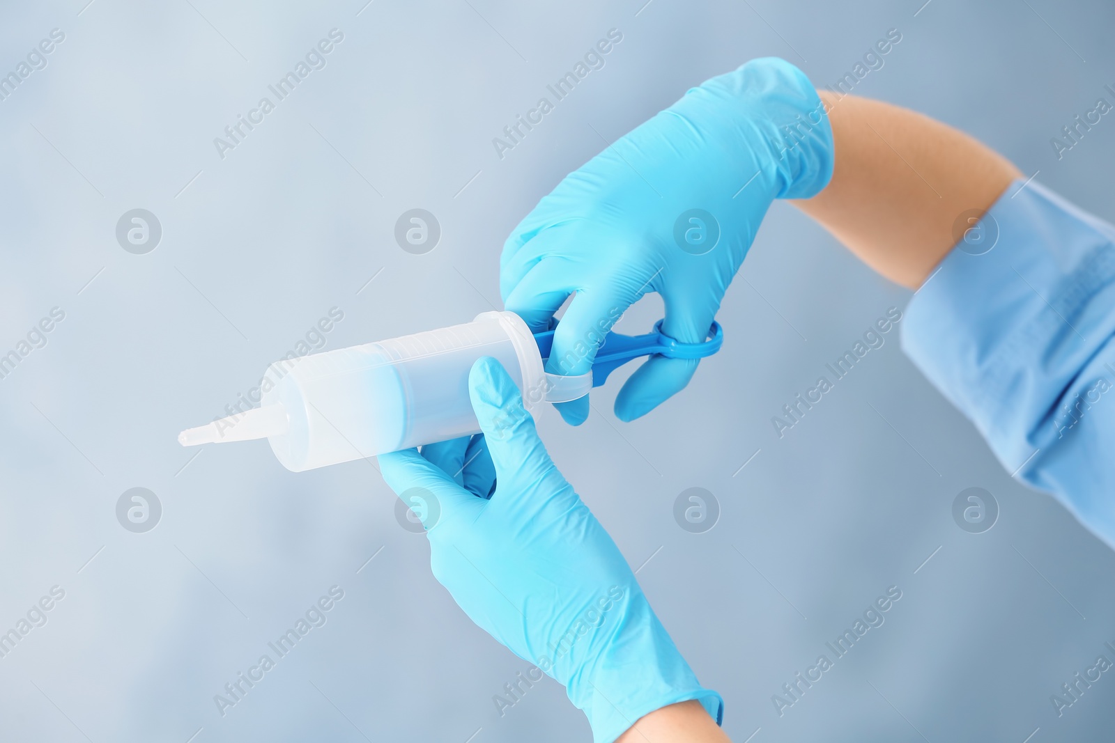 Photo of Doctor in medical gloves with large syringe on color background