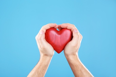 Man holding decorative heart in hands on color background, closeup