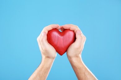 Photo of Man holding decorative heart in hands on color background, closeup