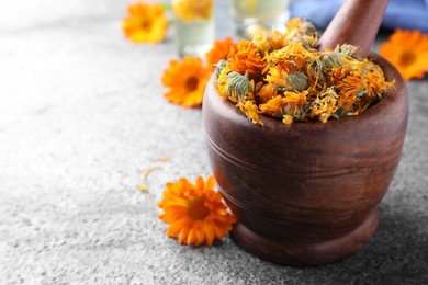 Photo of Wooden mortar with dry calendula flowers on light grey table, closeup. Space for text