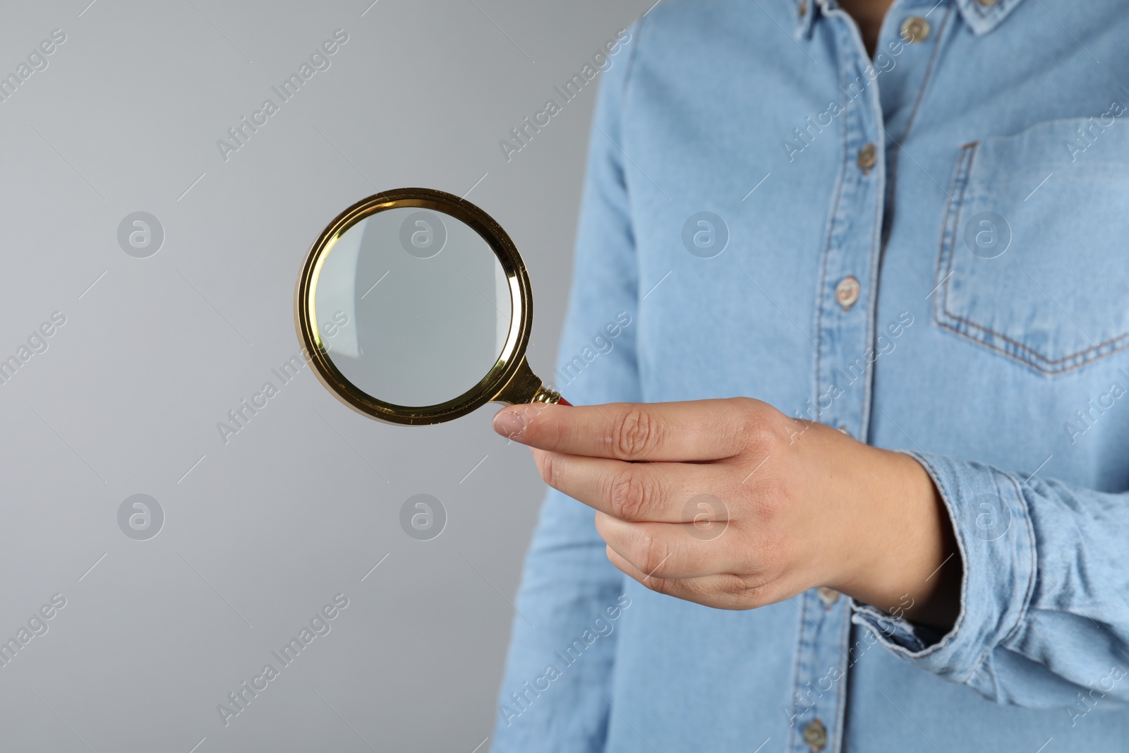 Photo of Woman holding magnifying glass on grey background, closeup. Find keywords concept