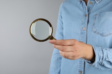 Photo of Woman holding magnifying glass on grey background, closeup. Find keywords concept