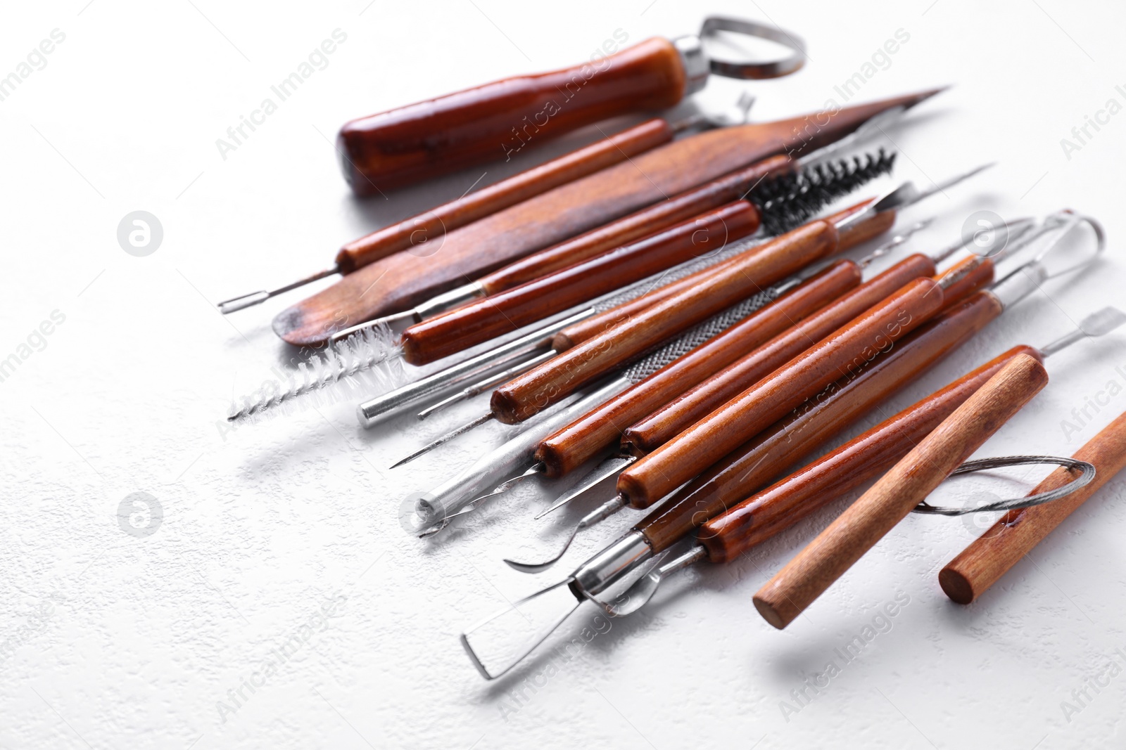 Photo of Set of different clay crafting tools on white textured table, closeup