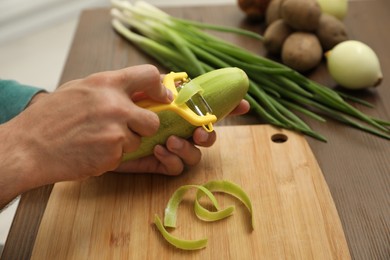 Photo of Man peeling zucchini at kitchen table, closeup. Preparing vegetable