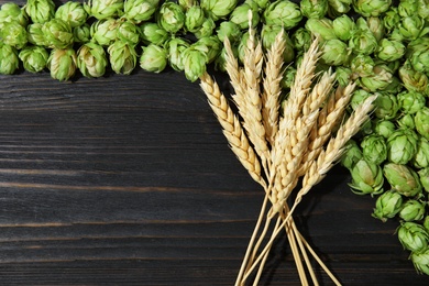 Fresh green hops and wheat spikes on wooden background, top view with space for text. Beer production