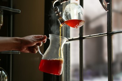 Barista pouring coffee from vacuum maker into glass jug in cafe, closeup. Space for text