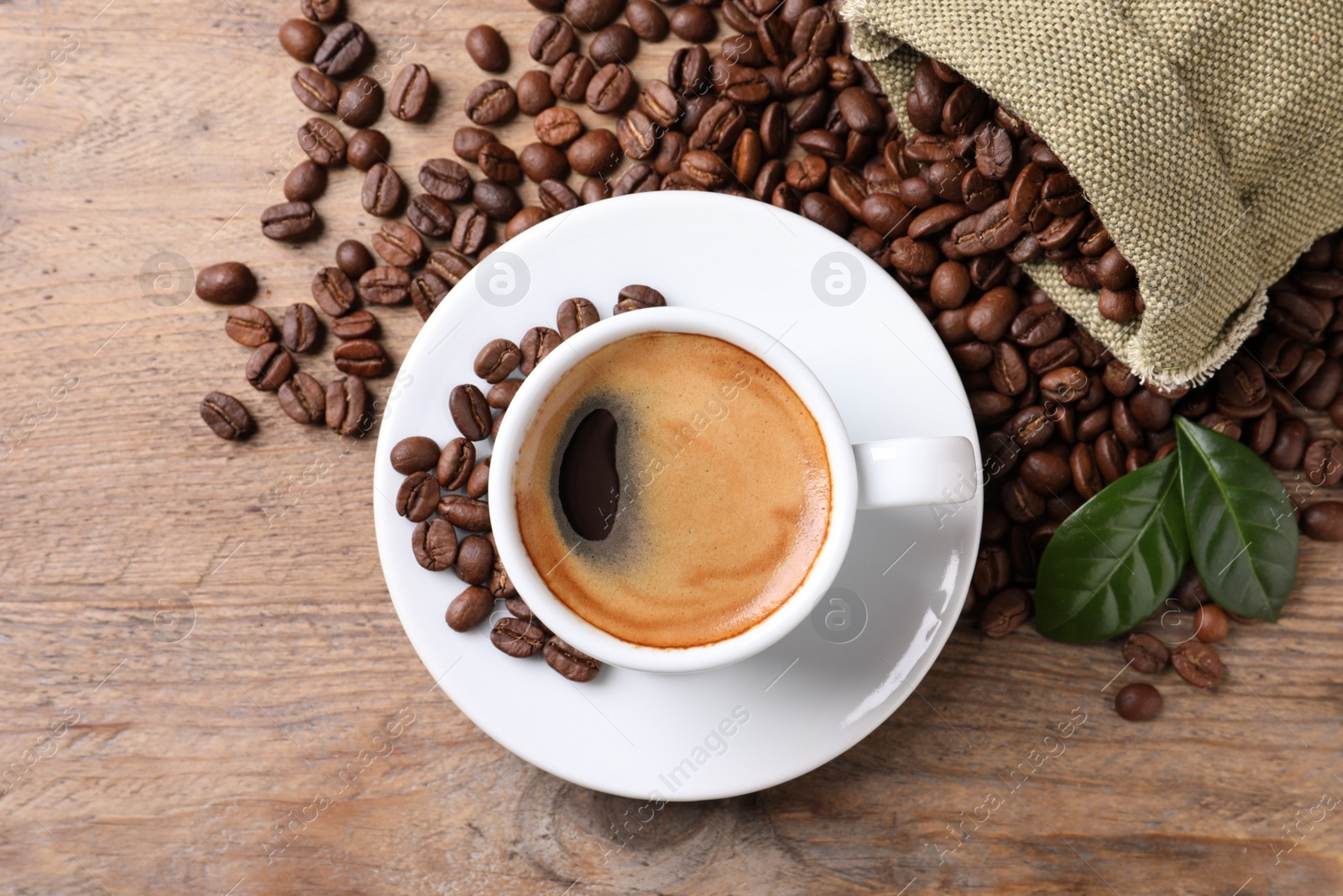 Photo of Cup of hot aromatic coffee and roasted beans on wooden table, flat lay