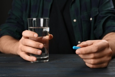 Man holding pill and glass of water at table, closeup