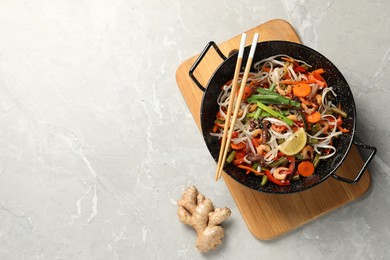 Photo of Shrimp stir fry with noodles and vegetables in wok on grey table, top view. Space for text