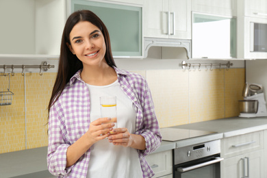 Beautiful young woman with lemon water in kitchen. Space for text