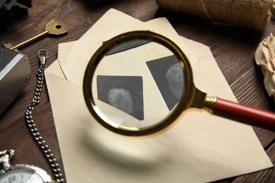 Photo of Magnifying glass  and fingerprints on wooden table, closeup. Detective's workplace
