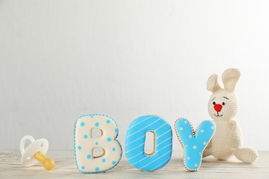 Word Boy made of tasty cookies, toy and pacifier on white wooden table. Baby shower party