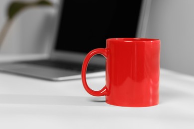 Red ceramic mug on table at workplace, space for text