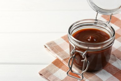 Tasty barbecue sauce in glass jar on white wooden table, closeup. Space for text