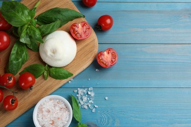 Delicious burrata cheese with basil and tomatoes on light blue wooden table, flat lay. Space for text