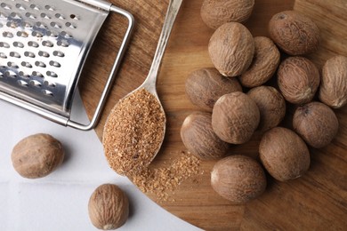 Photo of Spoon with grated nutmeg, seeds and grater on white table, flat lay
