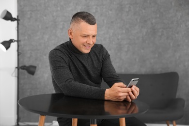 Photo of Mature man with mobile phone at table indoors
