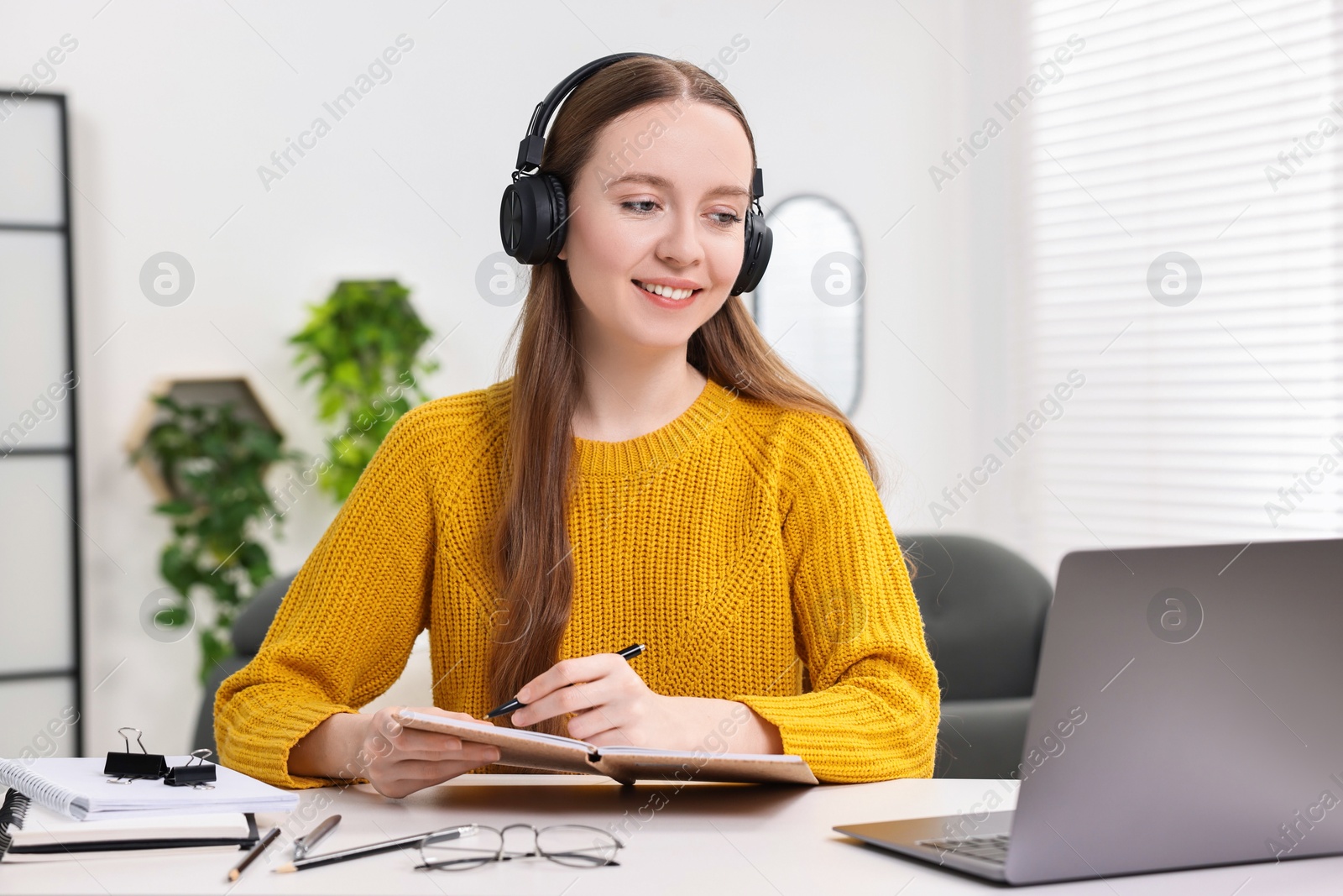 Photo of E-learning. Young woman taking notes during online lesson at white table indoors