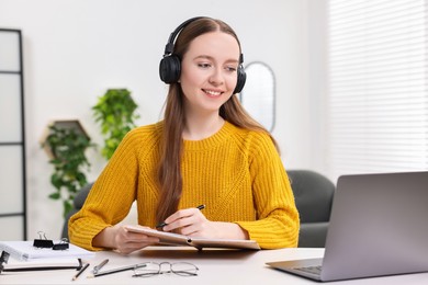 Photo of E-learning. Young woman taking notes during online lesson at white table indoors