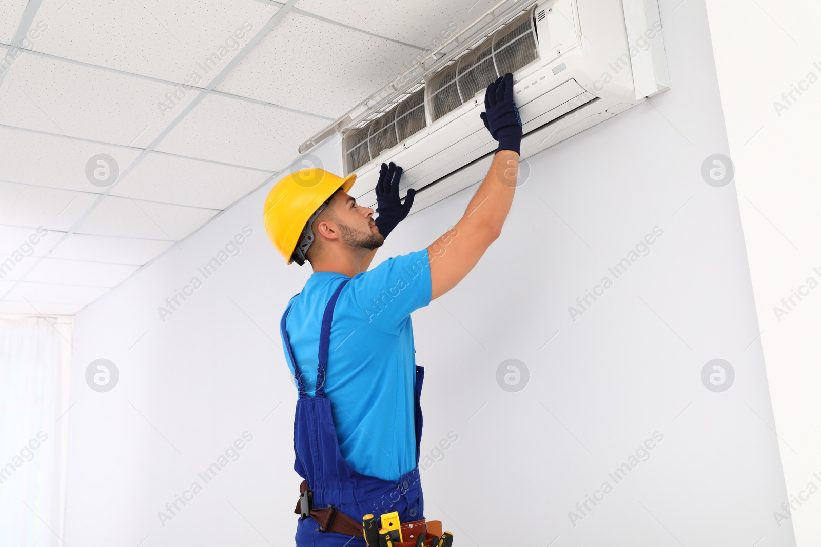 Photo of Professional technician maintaining modern air conditioner indoors