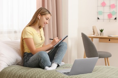 Photo of Teenage girl writing in notebook on bed at home