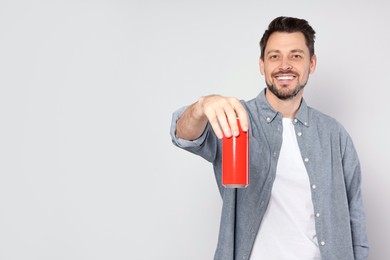 Photo of Happy man holding red tin can with beverage on light grey background. Space for text