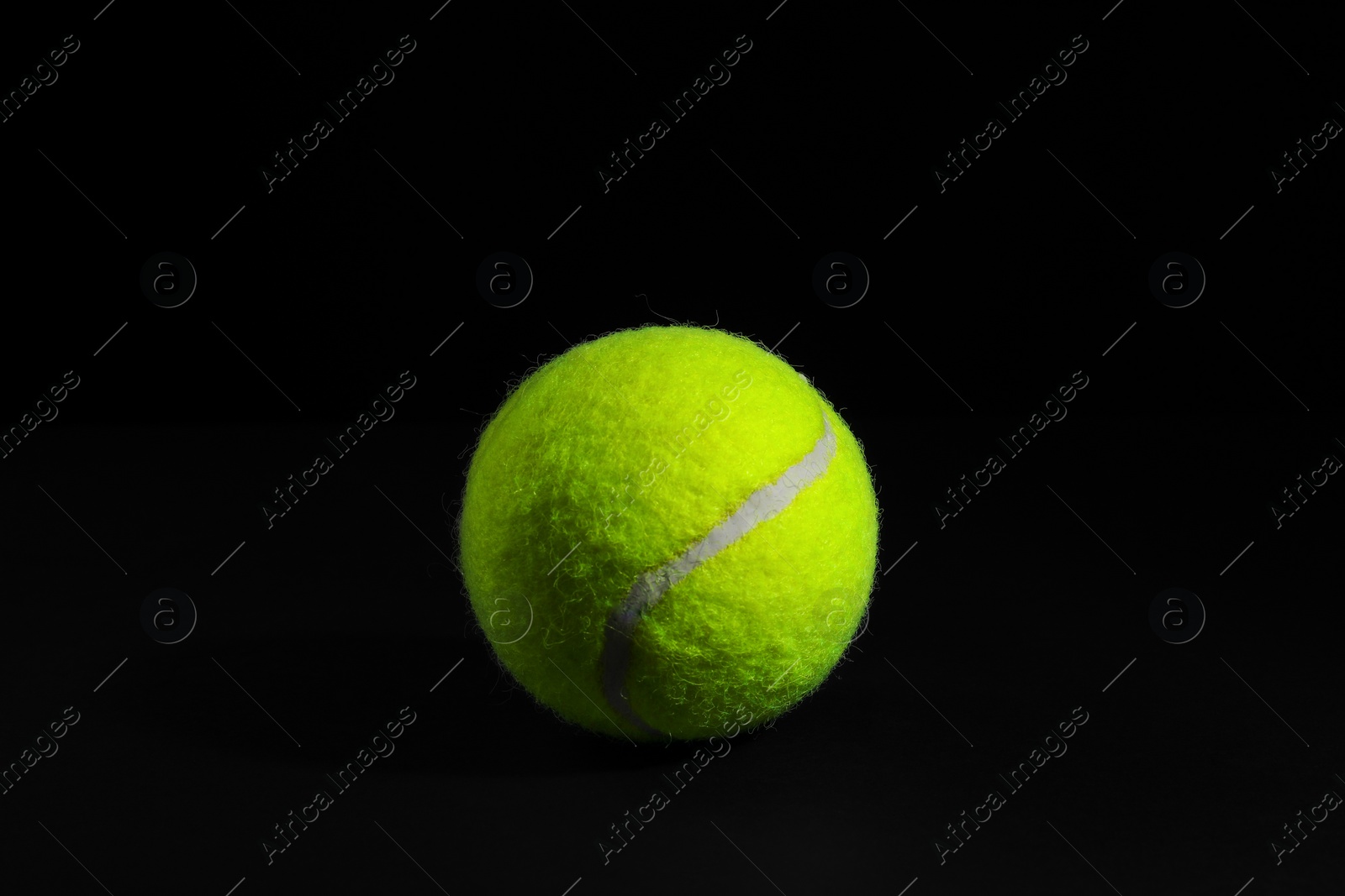 Photo of One bright tennis ball on black background