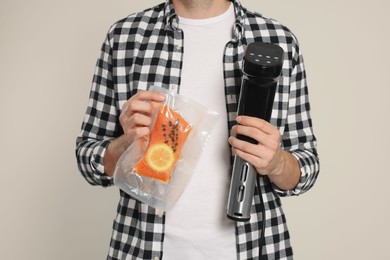 Man holding sous vide cooker and salmon in vacuum pack on beige background, closeup