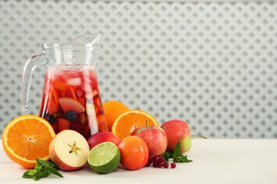 Photo of Jug of Red Sangria and fruits on white wooden table, space for text
