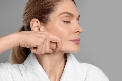 Photo of Woman massaging her face on grey background