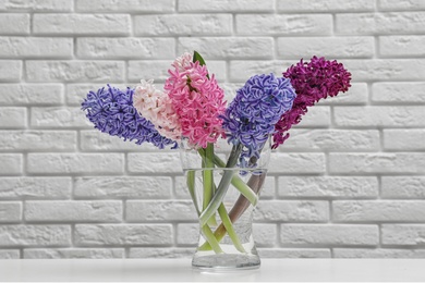 Photo of Beautiful hyacinths in glass vase on table against brick wall. Spring flowers