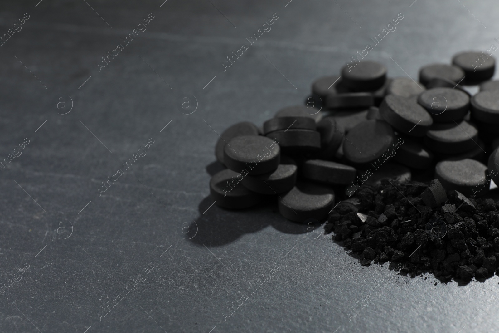 Photo of Activated charcoal pills on black table, closeup with space for text. Potent sorbent