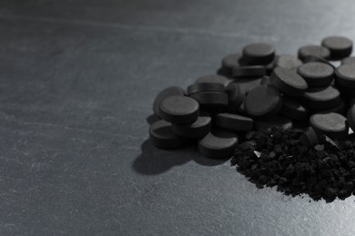 Photo of Activated charcoal pills on black table, closeup with space for text. Potent sorbent