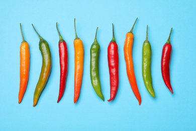 Different hot chili peppers on blue background, flat lay