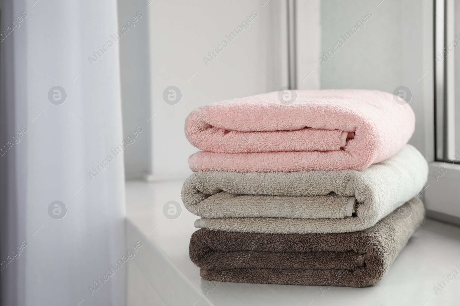 Photo of Stack of fresh towels on windowsill. Space for text