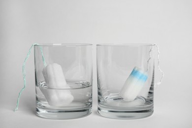 Photo of Tampons in glasses on light background. Comparison of absorption